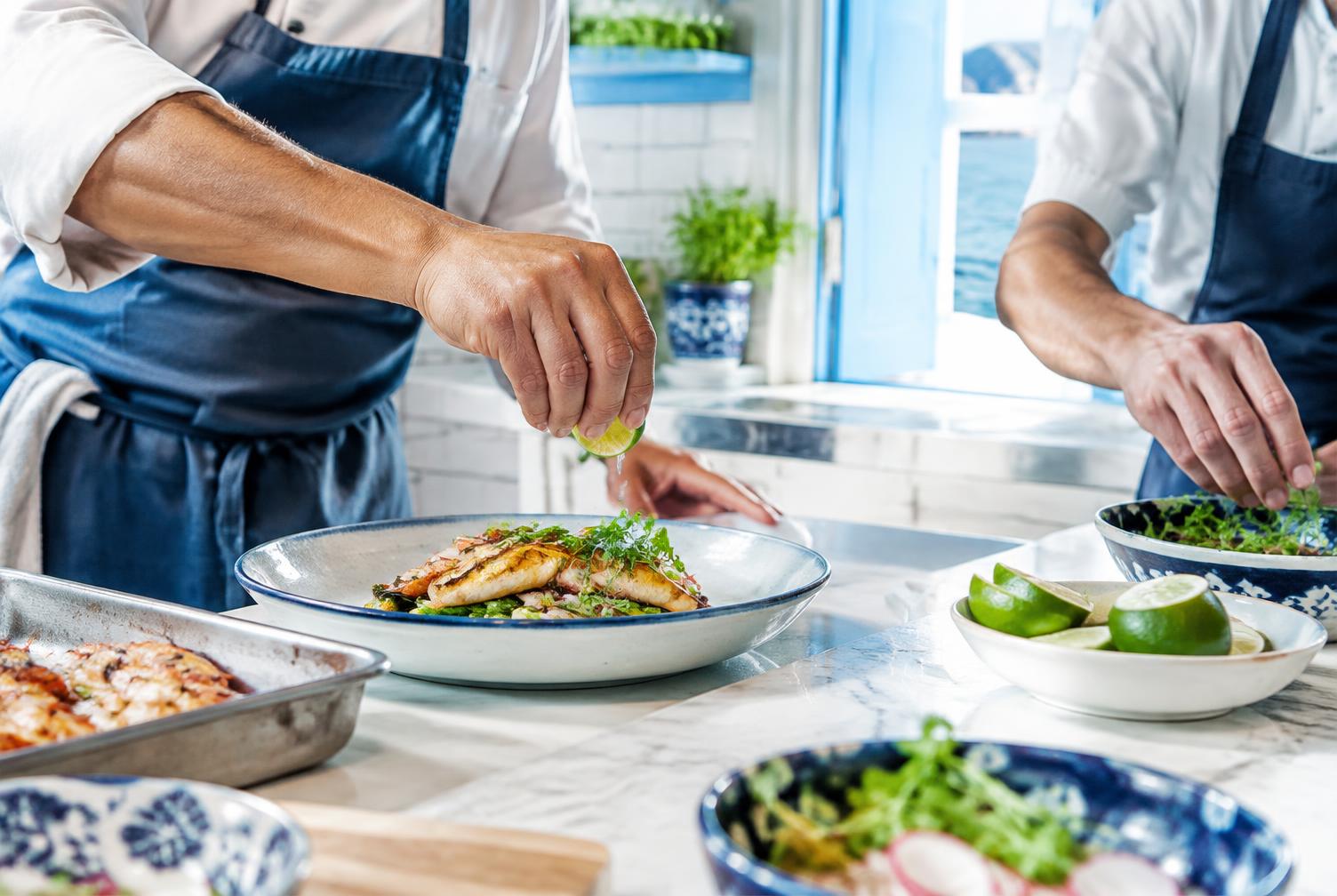 Chefs plating a fresh seafood dish in a bright coastal kitchen
